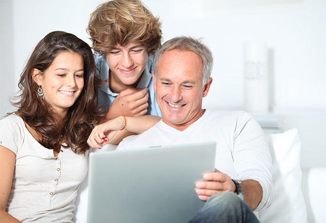 Man smiling whilst holding laptop showing screen to young male and female