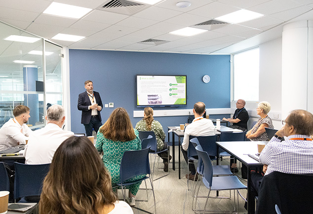 Classroom with adults sitting on tables and a man presenting 